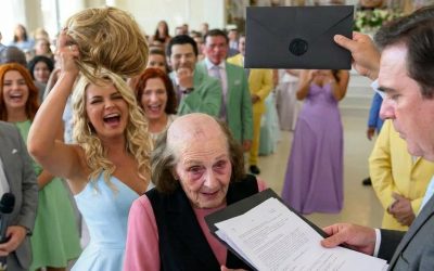 Mia nuora ha strappato la parrucca dalla testa di mia moglie al matrimonio di mio figlio. Quando ho aperto la busta che avevo portato, il sorriso della sposa è svanito. Mia nuora ha strappato la parrucca dalla testa di mia moglie durante il matrimonio di mio figlio, rivelando i segni lasciati da mesi di trattamento, mentre alcuni invitati ridevano. Sono salito sul palco, ho coperto mia moglie con la mia giacca e ho aperto la busta con gli inviti di nozze che avevo portato con me. Nel momento in cui la sposa ha visto i documenti all’interno, il suo sorriso è svanito. Jennifer ha alzato la mano verso la sommità della testa di Mary come se stesse semplicemente sistemando una ciocca di capelli. “Ecco, Mary”, ha detto dolcemente. “Lascia che te la sistemi io…” La sala da ballo profumava di fiori costosi, di un profumo intenso e di cibo caldo intatto su vassoi d’argento. Le luci del palcoscenico illuminavano l’abito da sposa di Jennifer, lo smoking impeccabile di Lucas e il volto esausto di mia moglie, che cercava di sorridere come se fosse una normale e felice festa di famiglia. Ma la vita di Mary non era stata normale per mesi. Aveva sopportato visite mediche, ecografie, ricoveri ospedalieri, moduli di trattamento firmati con mani tremanti, referti, scontrini piegati nella borsa e fazzoletti nascosti nel cassetto del comodino per non farmi vedere quanto spesso piangeva. Mary non si vergognava di essere malata. Voleva solo sopravvivere al matrimonio di suo figlio senza diventare il centro dei pettegolezzi. Jennifer lo sapeva. Anche Lucas lo sapeva. E in quel momento, capii una cosa con chiarezza: alcuni atti di crudeltà non sono casuali. Alcune persone si esercitano a sorridere prima di colpire. Le dita di Jennifer si chiusero attorno alla base della parrucca castana di mia moglie. Accadde in fretta. Con precisione. Con crudeltà. L’adesivo cedette con un suono secco e la parrucca si staccò completamente. Jennifer non la lasciò cadere. La sollevò come un trofeo, tenendo il microfono vicino alla bocca mentre l’intera sala piombava in un silenzio attonito. Le forchette si immobilizzarono a mezz’aria. Il bicchiere di una damigella tremò nella sua mano. Un cameriere vicino al tavolo degli sposi si fermò con il vassoio inclinato. Persino la musica sembrò soffocarsi prima di scomparire dagli altoparlanti. Sotto le luci bianche e intense, la testa nuda di Mary era esposta. Sottili ciocche grigie. Pelle segnata dalle cure. La dolorosa testimonianza di una donna che combatteva contro un cancro al terzo stadio. Per tre secondi, nessuno sembrò capire appieno cosa fosse successo. Poi qualcuno rise. “Oh mio Dio”, disse Jennifer al microfono, la sua finta innocenza tagliente come una lama. “Non immaginavo che si sarebbe staccata così facilmente!” Cercai Lucas con lo sguardo. Mio figlio era a pochi passi di distanza. Abbastanza vicino da fare un passo avanti. Abbastanza vicino da prendere la parrucca dalle mani della sposa. Abbastanza vicino da coprire sua madre, la donna che lo aveva portato in grembo, cresciuto, aspettato fuori dai cancelli della scuola, pagato la sua retta, portato di corsa al pronto soccorso e che ancora conservava i suoi disegni d’infanzia in una scatola blu in fondo al nostro armadio. Un solo movimento sarebbe bastato. Ma Lucas non si mosse. Il suo viso si fece rosso, non di rabbia verso Mary, ma di imbarazzo per colpa sua. Poi si voltò leggermente, come se abbandonare sua madre fosse più facile che affrontare i ricchi suoceri seduti in prima fila. Mary non urlò. Non pianse. Non implorò nessuno di aiutarla. Si limitò a portare entrambe le mani al petto, cercando di rannicchiarsi nell’abito azzurro pallido che aveva scelto perché Lucas una volta le aveva detto che quel colore le donava molto. Quello mi ha quasi spezzato il cuore. Non le risate, però. Non la crudeltà di Jennifer. Il silenzio di Mary. A volte l’umiliazione peggiore non emette alcun suono. Rimane semplicemente congelata dentro chi ha già sofferto troppo. Mi alzai dal mio posto. Le gambe della sedia stridevano rumorosamente sul pavimento, sovrastando le risate. Non corsi. Non gridai. Camminai lentamente verso il palco, con la calma di un uomo che aveva già preso la sua decisione prima ancora che iniziasse la serata. La folla si aprì. Salii i gradini, ignorai completamente Jennifer e mi tolsi la giacca blu scuro. Poi la posai sulle spalle tremanti di Mary e le coprii il capo con la massima delicatezza possibile. Lei alzò lo sguardo verso di me. Solo allora capii che il dolore più profondo non era nelle sue lacrime. Era nel modo in cui continuava a cercare suo figlio nella stanza. Presi il microfono dalle mani di Jennifer. «Mi scuso per aver interrotto il flusso della serata», dissi, la mia voce che risuonava sotto l’alto soffitto. «Ma visto che avete appena assistito a una donna malata trasformata in intrattenimento, è giusto che vediate anche il regalo di nozze che ho portato per mio figlio». Nella stanza calò un silenzio assoluto. Jennifer sorrideva ancora, ma ora il sorriso sembrava bloccato, come se temesse di svanire. Mi voltai verso Lucas. «Lucas», dissi, «ti ho portato un regalo stasera». Finalmente mi guardò. Infilai la mano nella tasca interna della camicia ed estrassi una spessa busta nera sigillata con ceralacca. Non era un biglietto d’auguri. Non erano soldi. Non era il tipo di regalo che si apre tra champagne e torta. Avevo preparato quella busta sei mesi prima, lo stesso giorno in cui…A Kek Mary è stata diagnosticata una malattia terminale. Alle 9:15 di martedì mattina, dopo essere uscita dall’ospedale, mi sono seduta con un avvocato e ho esaminato i documenti relativi alla procura, agli estratti conto, agli atti di proprietà, alle clausole previdenziali e alle direttive anticipate di trattamento. Non per vendetta. Per protezione. Perché la protezione è ciò che diventa l’amore quando la crudeltà inizia a tramare. Ho rotto il sigillo di ceralacca. I documenti sono scivolati fuori, pesanti e precisi: firmati, datati, autenticati, timbrati e disposti nell’esatto ordine in cui li avevo preparati. Gli ospiti in prima fila si sono sporsi in avanti. La madre di Jennifer sembrò trattenere il respiro per un istante. Lucas fece un piccolo passo, quasi impercettibile, come se avesse finalmente capito che quella busta non apparteneva alla festa. Jennifer cercò di ridere. “Che drammaticità”, mormorò. Non la guardai. Ho semplicemente girato la prima pagina in modo che Lucas potesse leggere il titolo. E quando Jennifer vide le prime parole stampate sul documento all’interno di quella busta nuziale, il suo sorriso svanì come se qualcuno avesse spento la luce dietro il suo viso. Ciò che era scritto lì cambiò tutto ciò che Lucas credeva di possedere. Storia completa nel primo commento ⬇️